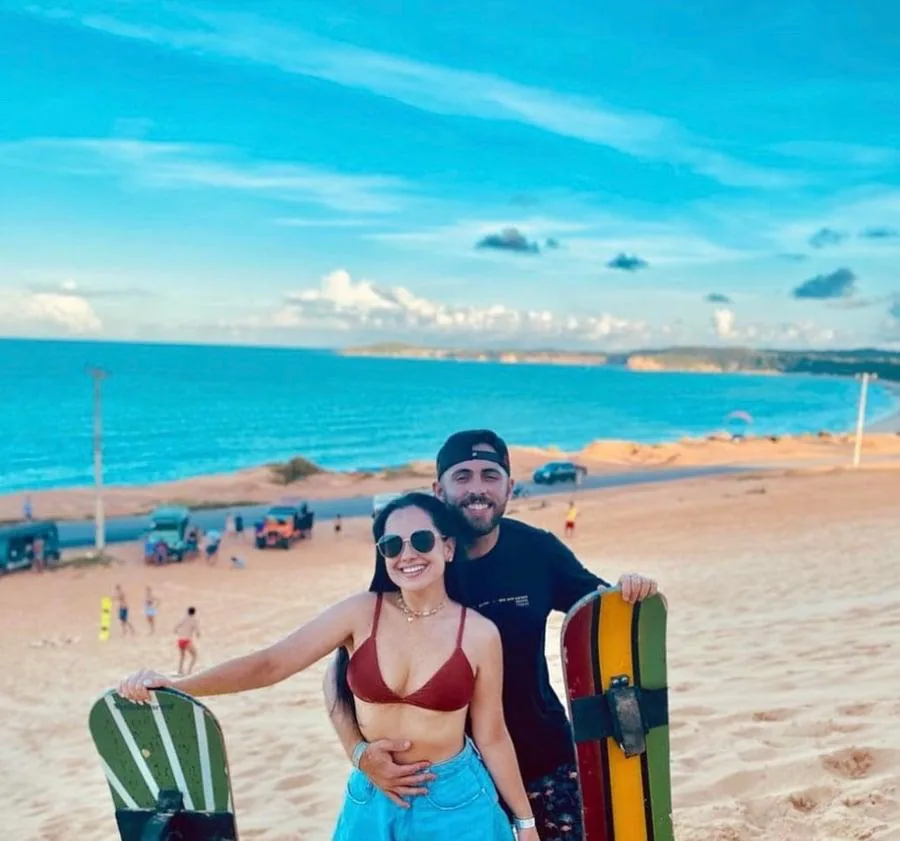 Casal praticando sandboard nas dunas
